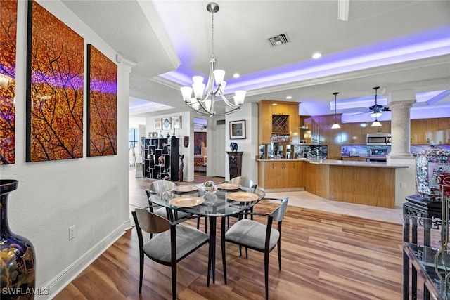 dining room with visible vents, light wood finished floors, a raised ceiling, a chandelier, and ornate columns