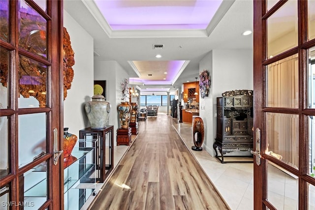 corridor with a tray ceiling, recessed lighting, visible vents, and light wood finished floors