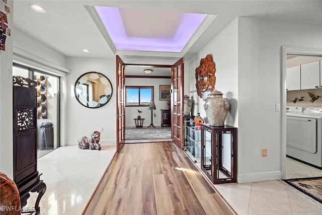 hallway with a tray ceiling, light wood-style flooring, baseboards, and independent washer and dryer