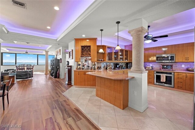 kitchen with appliances with stainless steel finishes, light wood-type flooring, tasteful backsplash, a tray ceiling, and pendant lighting