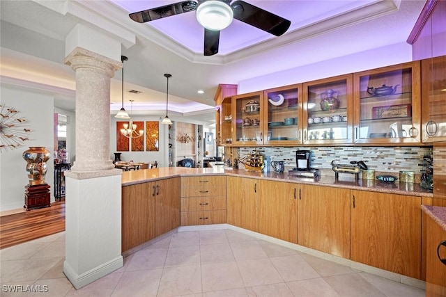 kitchen with a tray ceiling, decorative columns, a peninsula, and ornamental molding