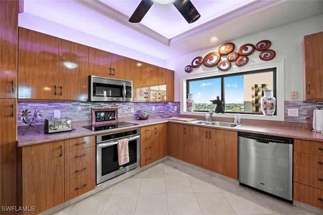 kitchen featuring tasteful backsplash, a tray ceiling, appliances with stainless steel finishes, a ceiling fan, and a sink