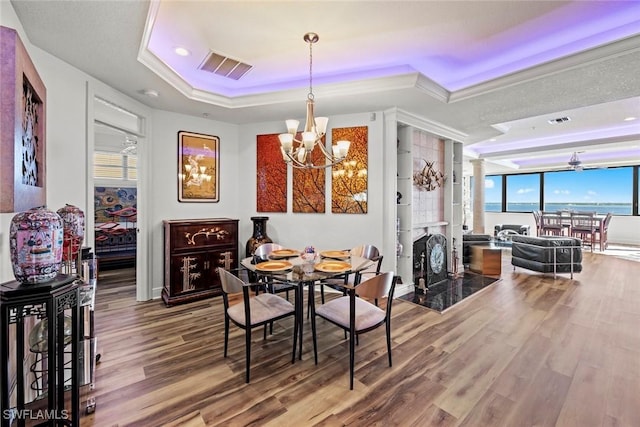 dining space featuring a raised ceiling, a water view, a chandelier, and hardwood / wood-style flooring