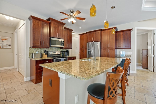 kitchen featuring stainless steel appliances, an island with sink, ceiling fan, hanging light fixtures, and a breakfast bar area