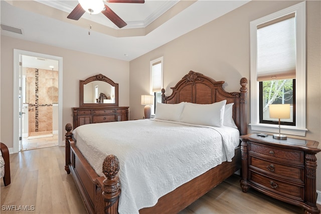 bedroom featuring light wood-type flooring, a tray ceiling, ceiling fan, and connected bathroom