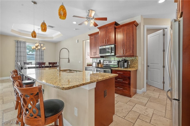 kitchen featuring ceiling fan with notable chandelier, pendant lighting, a kitchen island with sink, stainless steel appliances, and sink