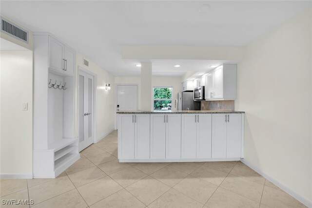 kitchen with light tile patterned floors, stone counters, stainless steel appliances, white cabinetry, and kitchen peninsula