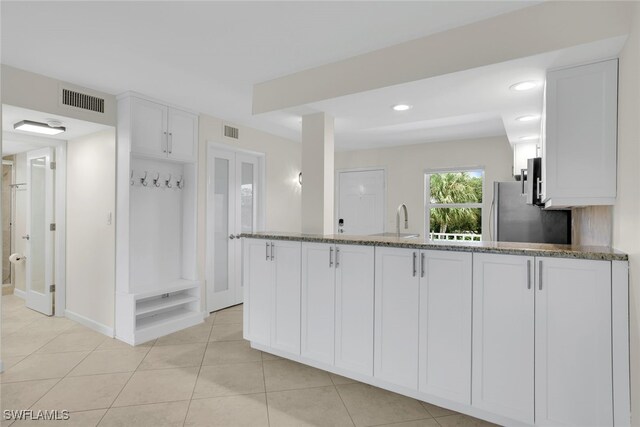 kitchen with white cabinets, stainless steel fridge, stone countertops, and sink