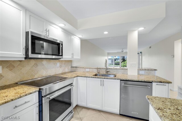 kitchen with light stone countertops, stainless steel appliances, sink, kitchen peninsula, and white cabinets