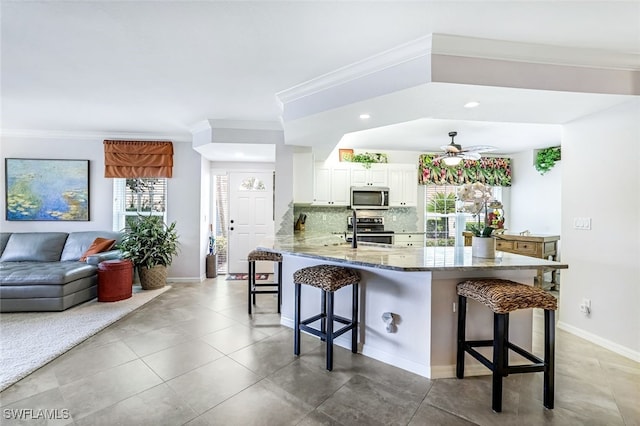 kitchen featuring kitchen peninsula, ceiling fan, a breakfast bar, appliances with stainless steel finishes, and white cabinets