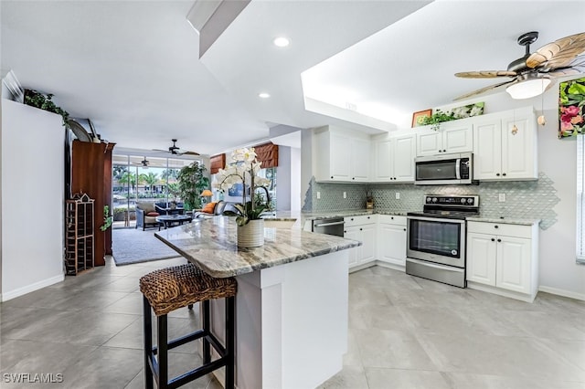 kitchen with appliances with stainless steel finishes, light stone counters, kitchen peninsula, and ceiling fan