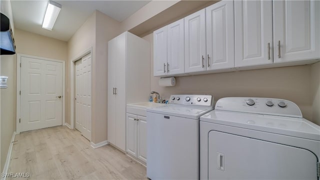 laundry area featuring cabinet space, washing machine and dryer, a sink, light wood-type flooring, and baseboards