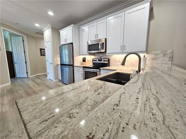 kitchen featuring white cabinetry, appliances with stainless steel finishes, light stone counters, and a sink