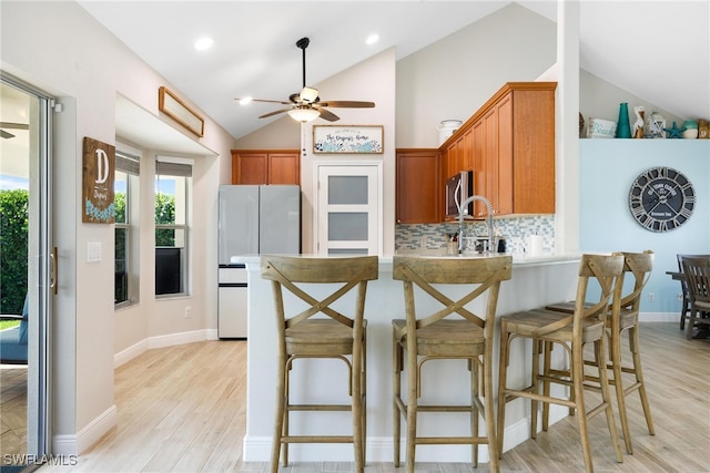 kitchen with white refrigerator, backsplash, kitchen peninsula, lofted ceiling, and light wood-type flooring