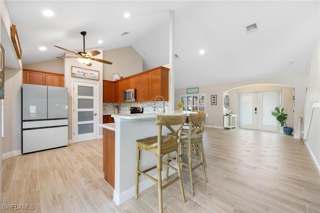 kitchen featuring a kitchen breakfast bar, light hardwood / wood-style flooring, high vaulted ceiling, kitchen peninsula, and white fridge