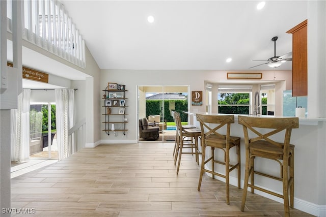 kitchen featuring a kitchen bar, ceiling fan, light hardwood / wood-style floors, and vaulted ceiling