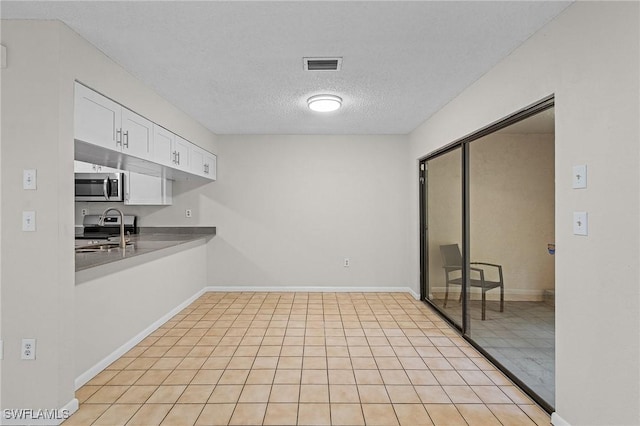 kitchen with sink, light tile patterned floors, a textured ceiling, white cabinetry, and stainless steel appliances