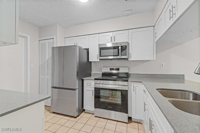 kitchen with white cabinets, appliances with stainless steel finishes, light tile patterned flooring, and sink