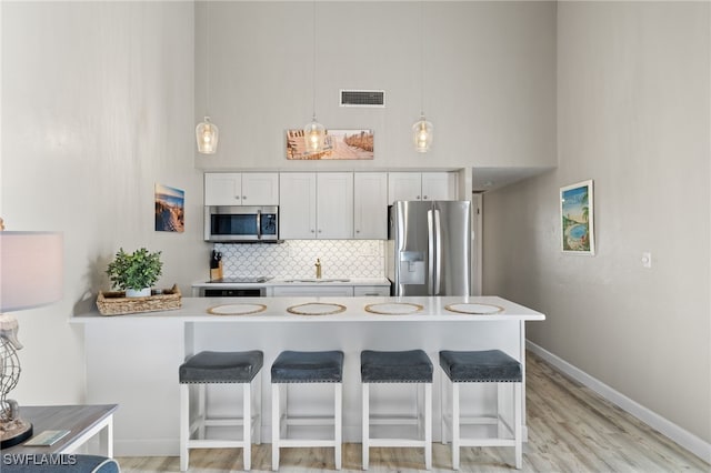 kitchen with decorative light fixtures, stainless steel appliances, a kitchen bar, and white cabinetry