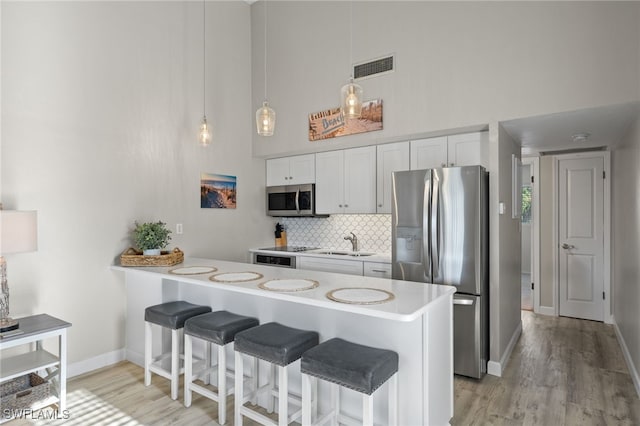 kitchen with sink, kitchen peninsula, white cabinetry, appliances with stainless steel finishes, and a breakfast bar