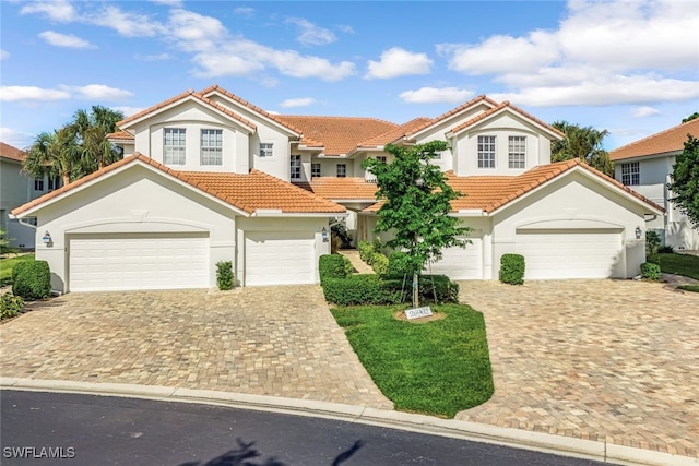 mediterranean / spanish-style home featuring an attached garage, a tile roof, decorative driveway, and stucco siding