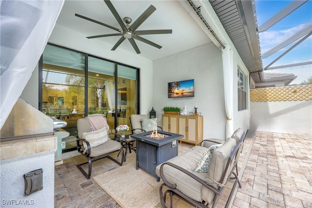 view of patio featuring glass enclosure, ceiling fan, and an outdoor fire pit