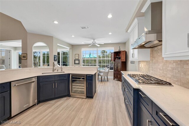 kitchen featuring appliances with stainless steel finishes, white cabinetry, wine cooler, wall chimney exhaust hood, and sink