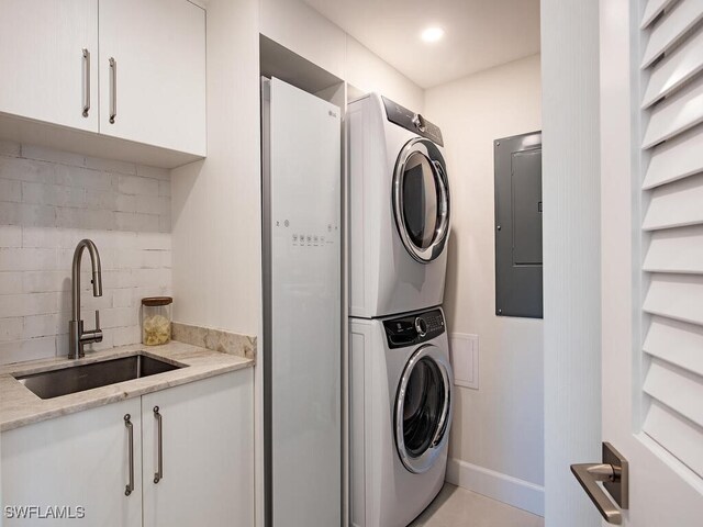 clothes washing area with cabinets, stacked washer / dryer, electric panel, and sink