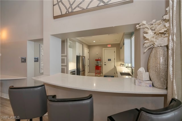 kitchen with sink, kitchen peninsula, stainless steel fridge, crown molding, and a kitchen bar