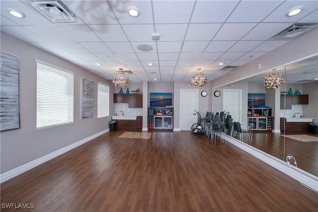 exercise room with a paneled ceiling, an inviting chandelier, and dark wood-type flooring