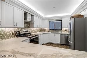 kitchen with light stone counters, white cabinets, stainless steel appliances, and wall chimney range hood