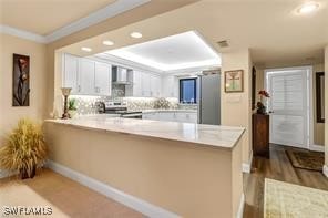 kitchen with white cabinets, wall chimney exhaust hood, a peninsula, crown molding, and stainless steel range with electric stovetop