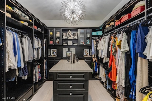 walk in closet with light hardwood / wood-style flooring and an inviting chandelier