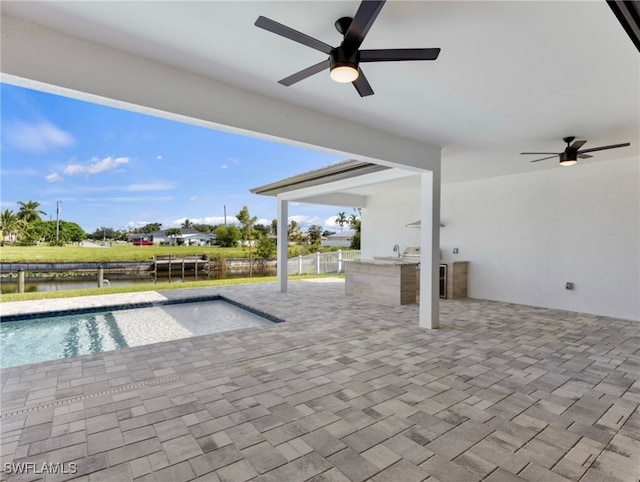 view of pool with sink, a water view, ceiling fan, exterior kitchen, and a patio area