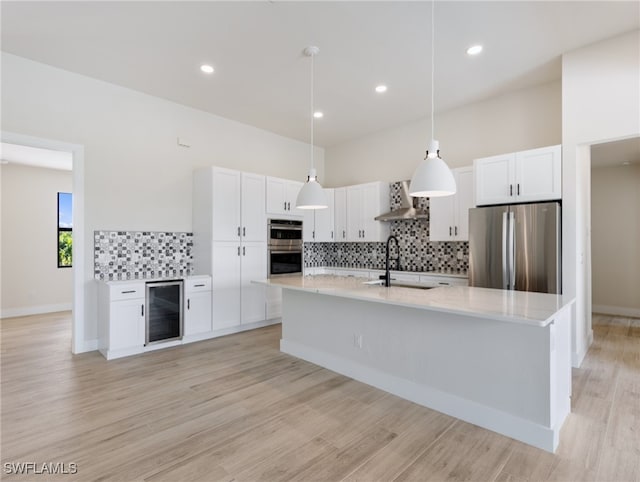 kitchen with appliances with stainless steel finishes, hanging light fixtures, beverage cooler, white cabinets, and wall chimney range hood