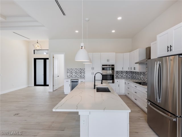 kitchen with stainless steel appliances, a center island with sink, pendant lighting, sink, and white cabinetry