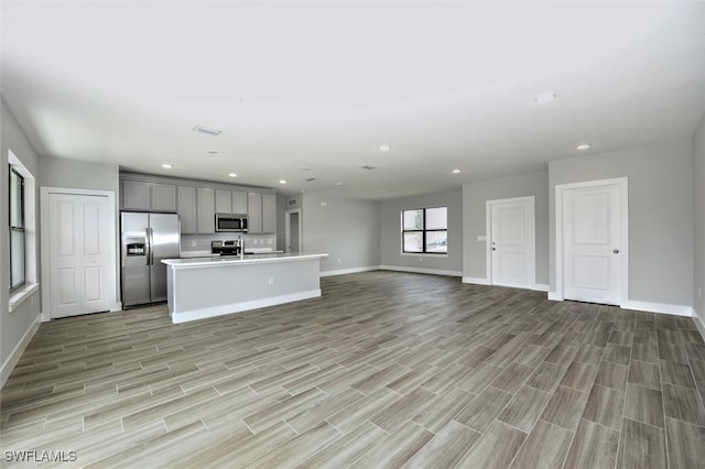 kitchen featuring appliances with stainless steel finishes, gray cabinetry, and a center island with sink