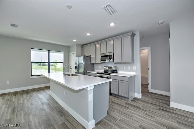 kitchen with sink, a center island with sink, gray cabinetry, and stainless steel appliances