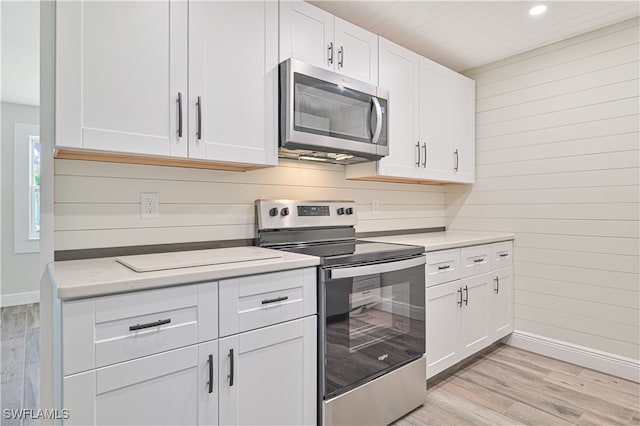 kitchen with wooden walls, white cabinets, light wood-type flooring, and appliances with stainless steel finishes