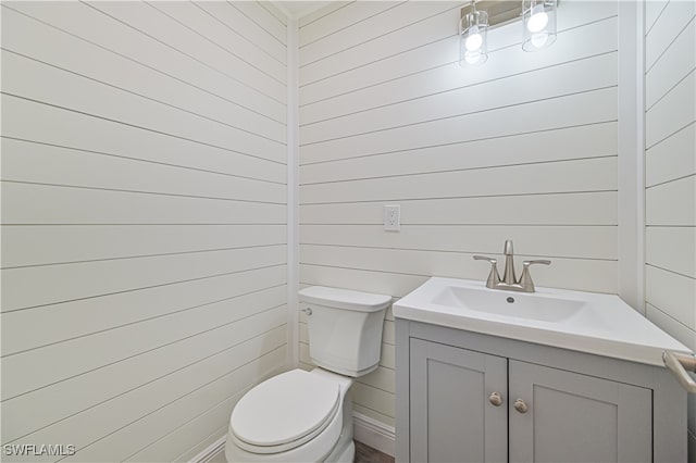 bathroom with wooden walls, vanity, and toilet