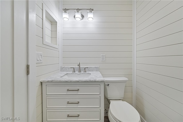 bathroom featuring vanity, toilet, and wood walls