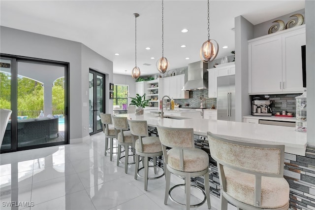 kitchen with a kitchen island with sink, pendant lighting, a kitchen bar, sink, and wall chimney exhaust hood