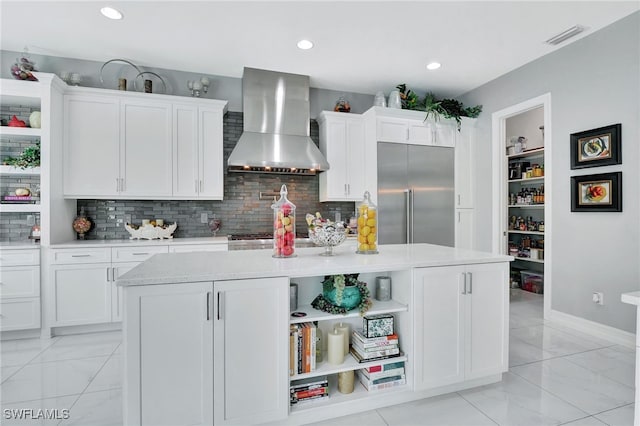 kitchen featuring white cabinetry, a center island, decorative backsplash, appliances with stainless steel finishes, and wall chimney range hood