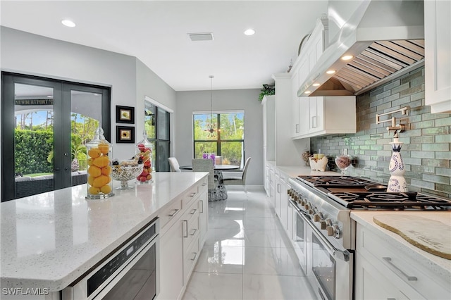 14690 Reserve Pl, Naples, FL 34109 - kitchen with double oven range, wall chimney exhaust hood, tasteful backsplash, white cabinets, and a kitchen island