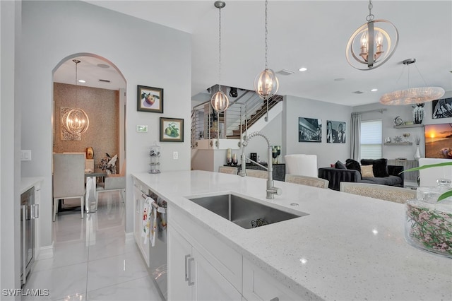 14690 Reserve Pl, Naples, FL 34109 - kitchen featuring a chandelier, a sink, light stone counters, arched walkways, and white cabinets