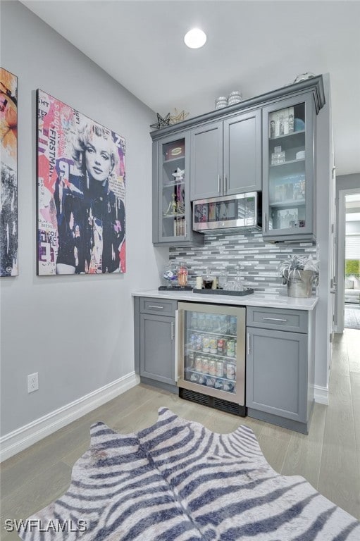 bar featuring gray cabinetry, wine cooler, tasteful backsplash, and light hardwood / wood-style floors