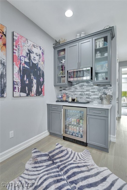 14690 Reserve Pl, Naples, FL 34109 - indoor bar featuring stainless steel microwave, beverage cooler, tasteful backsplash, and baseboards