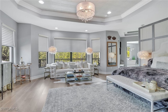 bedroom with light wood-type flooring, multiple windows, an inviting chandelier, and a tray ceiling