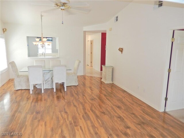 unfurnished dining area featuring ceiling fan with notable chandelier, vaulted ceiling, and hardwood / wood-style floors