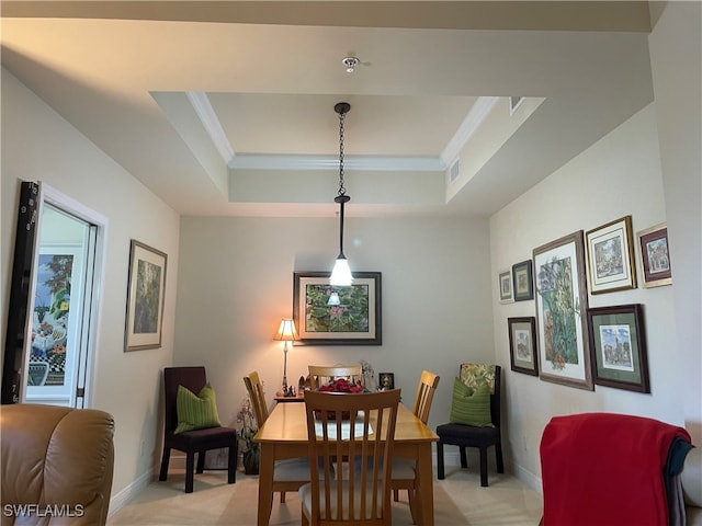 dining area with a raised ceiling, ornamental molding, and light carpet